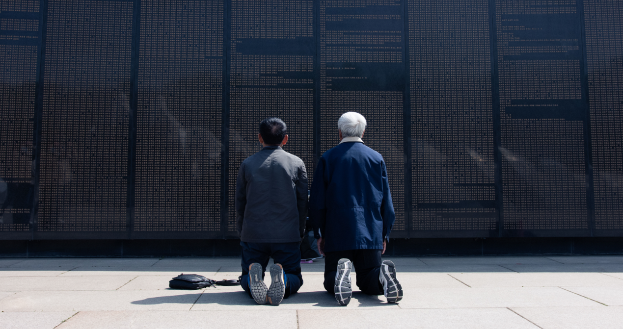 金伍星、金云星兄弟跪在补刻父亲名字后的烈士英名墙下。人民网记者 邱宇哲摄