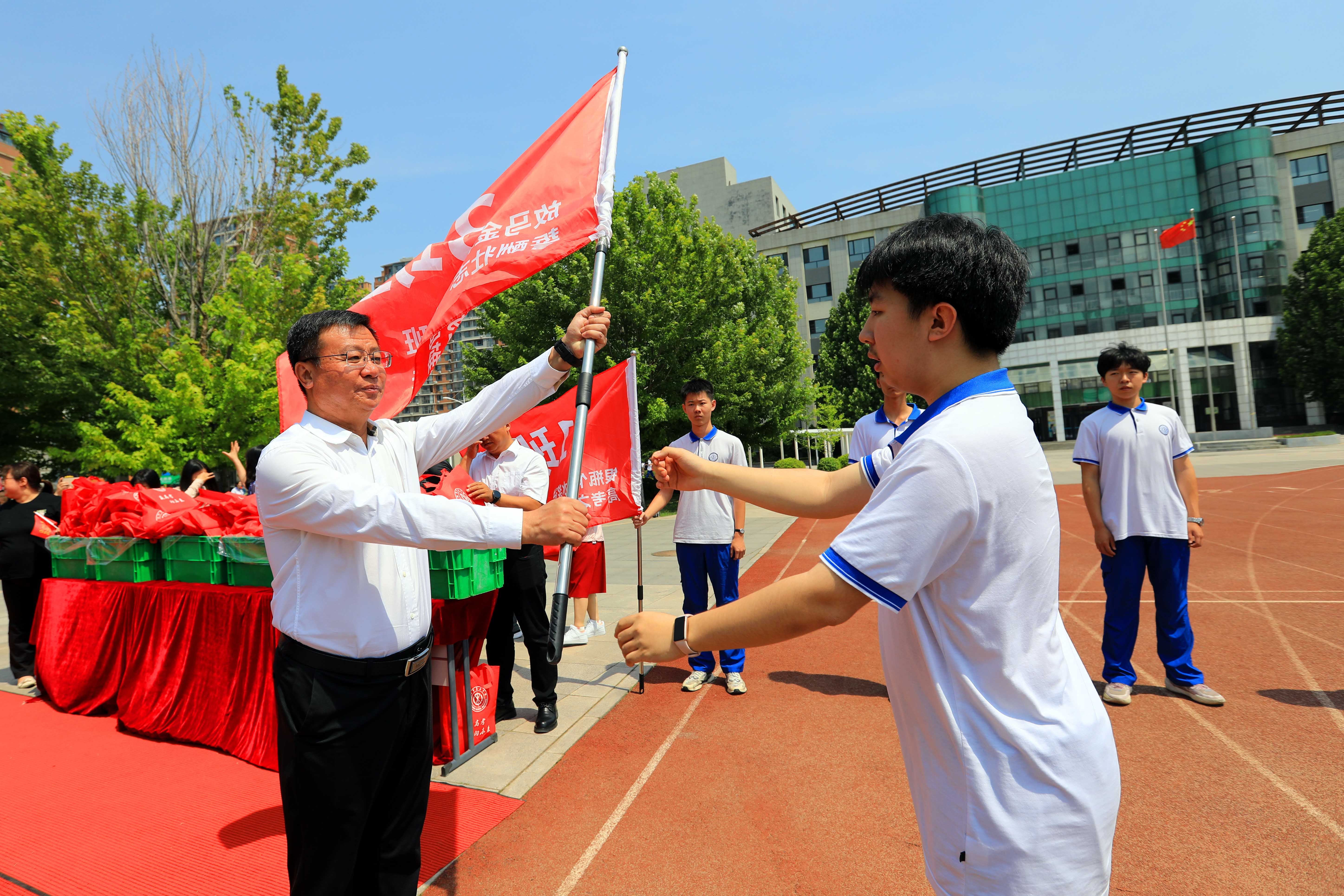 在通道的尽头，校长王新宇将高三班级的班旗传递给2025届高考班级代表，象征着把拼搏、努力、担当的精神一直传递下去。