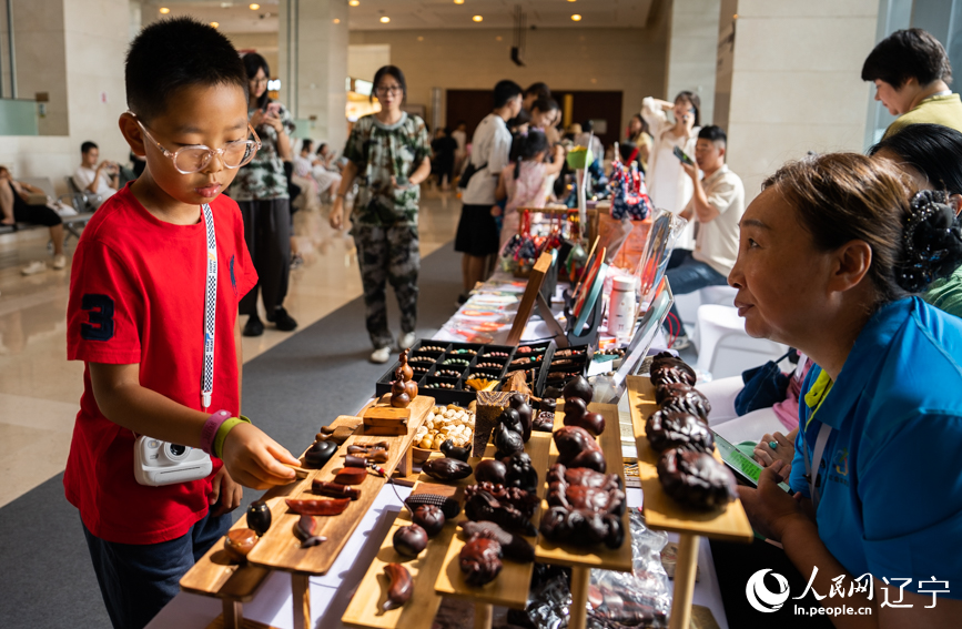 2025辽宁省非遗夏季博览会现场，小朋友把玩木雕手工艺品。人民网记者 邱宇哲摄