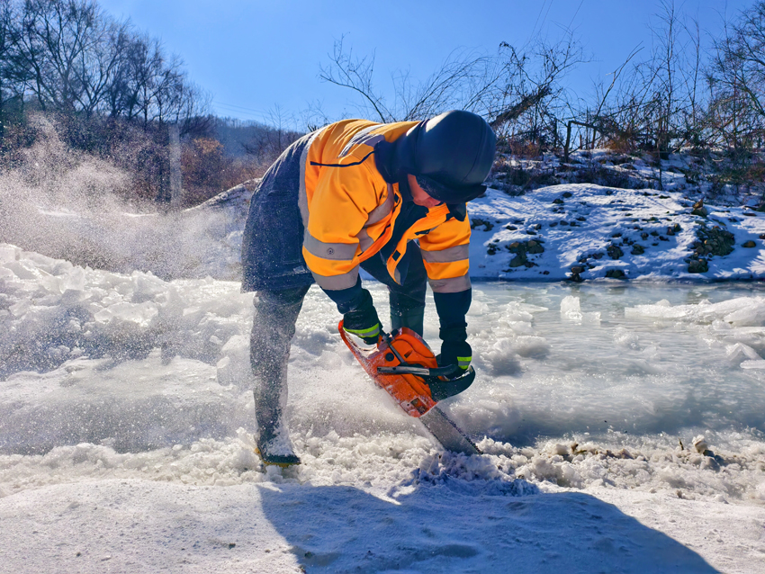 作业人员使用油锯切开河道内冰面，作为上游流水的引水槽。人民网记者 孝媛摄